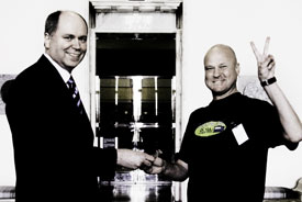 Vaalien häviäjä ja voittaja hymyssä suin. Keskellä sadan euron seteli.