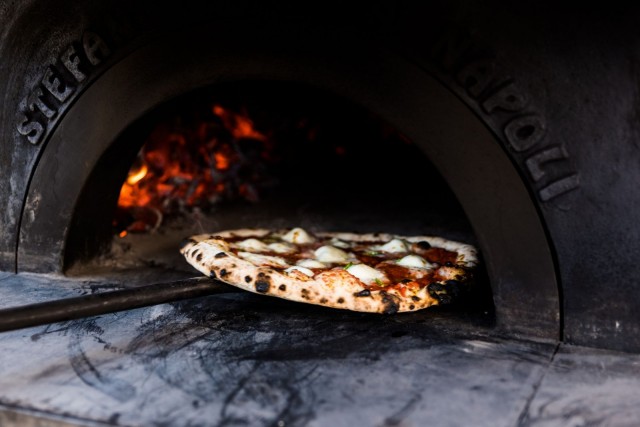 Käsintehty puu-uuni lämpenee 500-asteiseksi ja paistaa pizzan rapeaksi hetkessä.